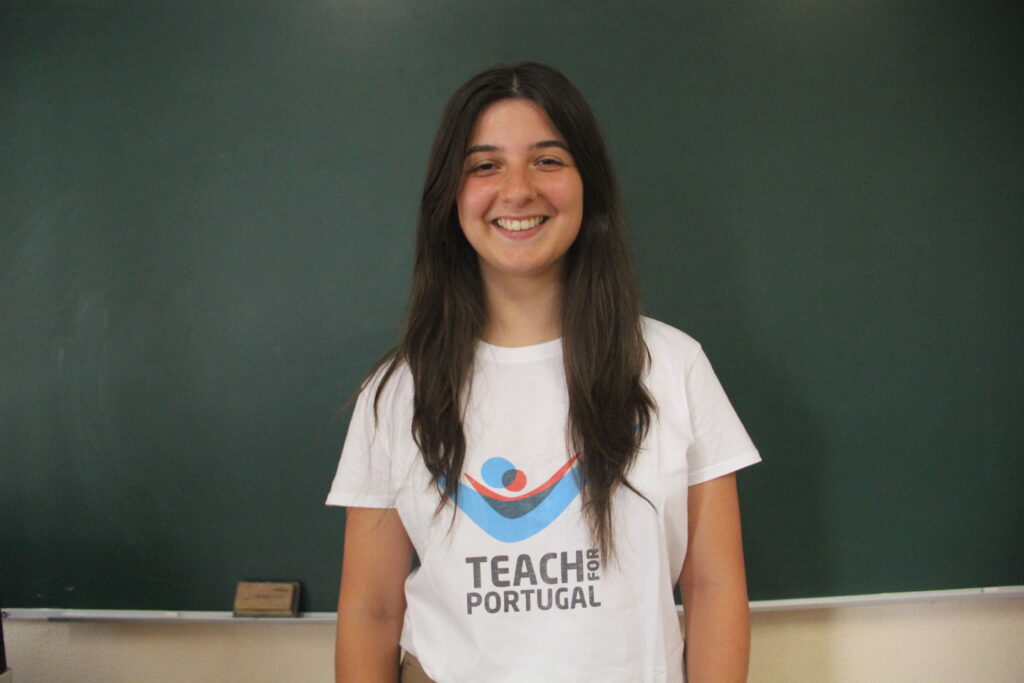Ana Rita Oliveira, Mentora 5ª Geração Teach For Portugal a usar a camisola com o logótipo da Teach For Portugal com um quadro de ardósia como fundo