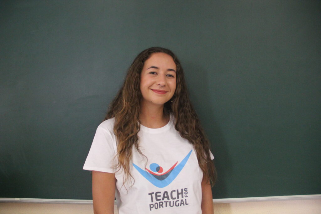 Cátia Almeida, Mentora 5ª Geração Teach For Portugal a usar a camisola com o logótipo da Teach For Portugal com um quadro de ardósia como fundo