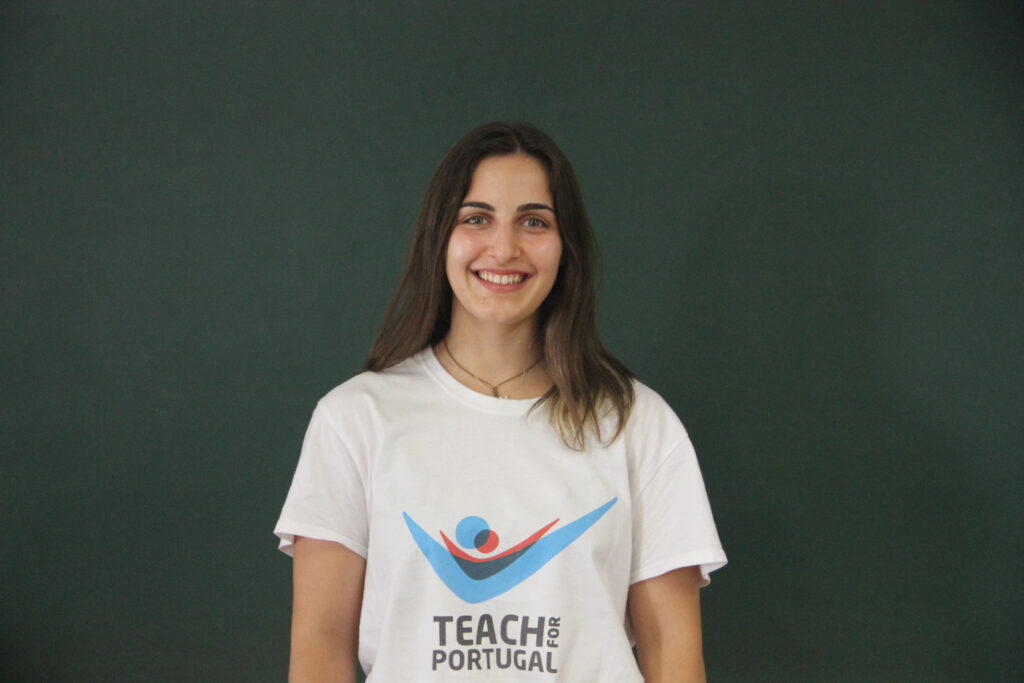 Sara Pinto, Mentora 5ª Geração Teach For Portugal a usar a camisola com o logótipo da Teach For Portugal com um quadro de ardósia como fundo