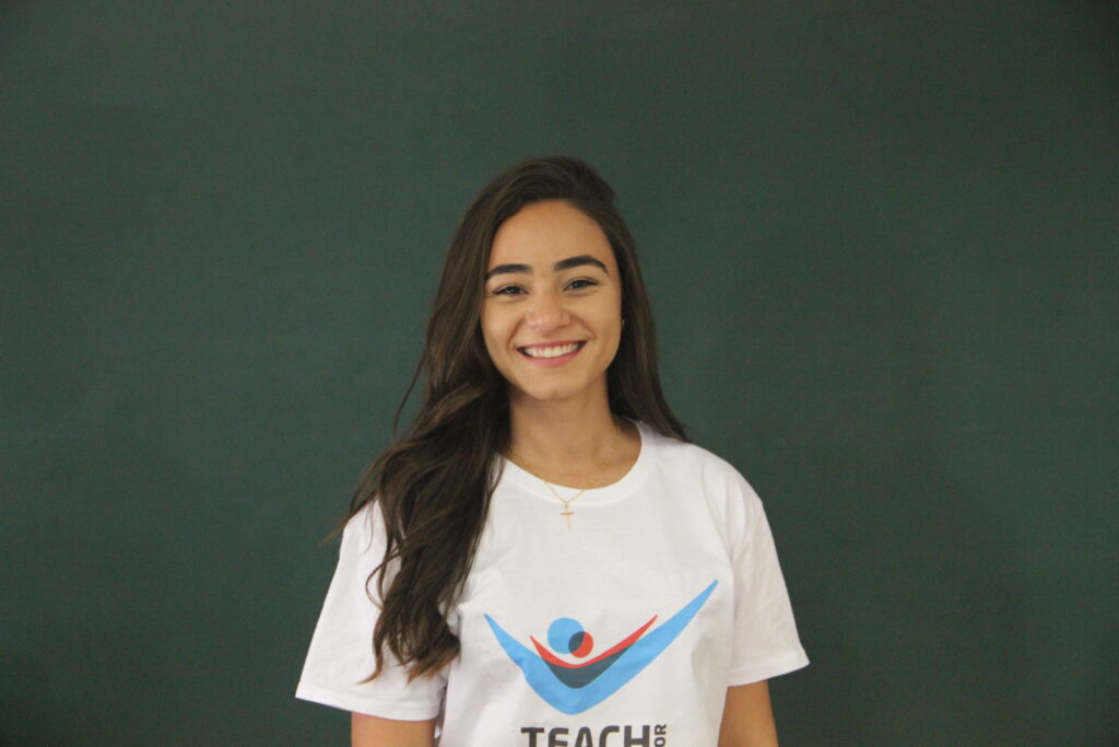 Isabella Ferreira, Mentora 5ª Geração Teach For Portugal a usar a camisola com o logótipo da Teach For Portugal com um quadro de ardósia como fundo