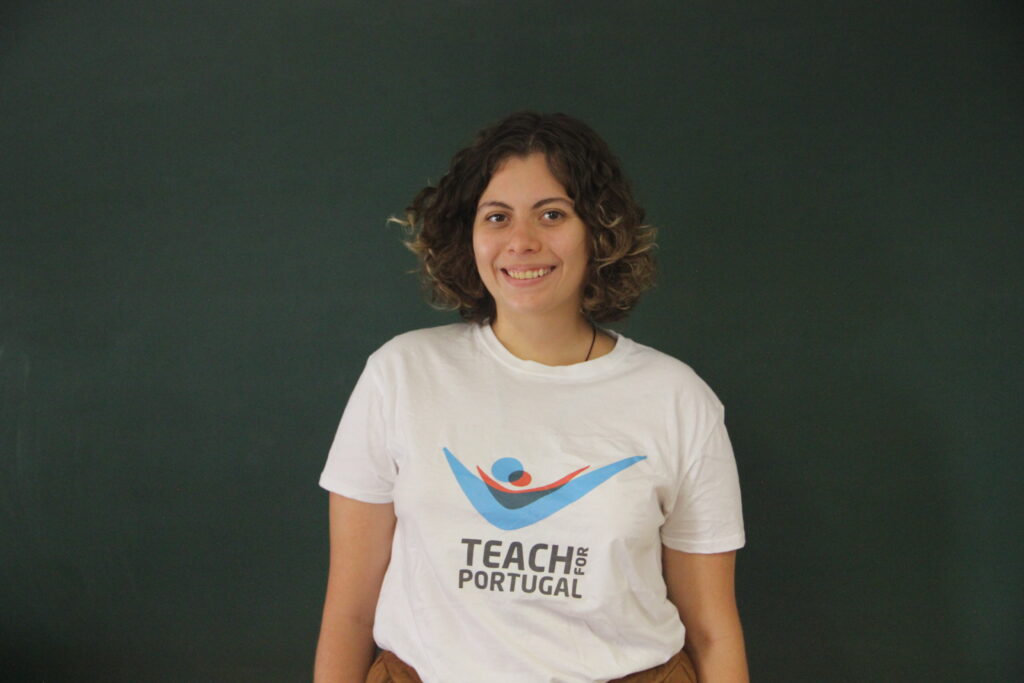 Stefanie Santos, Mentora 5ª Geração Teach For Portugal a usar a camisola com o logótipo da Teach For Portugal com um quadro de ardósia como fundo