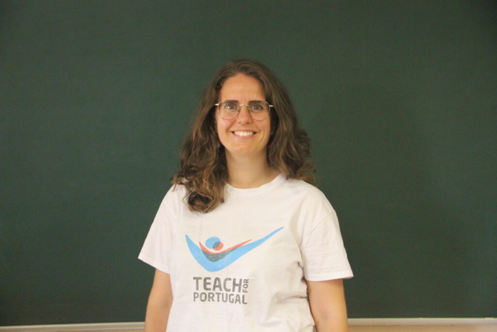 Daniela Pacheco, Mentora 5ª Geração Teach For Portugal a usar a camisola com o logótipo da Teach For Portugal com um quadro de ardósia como fundo