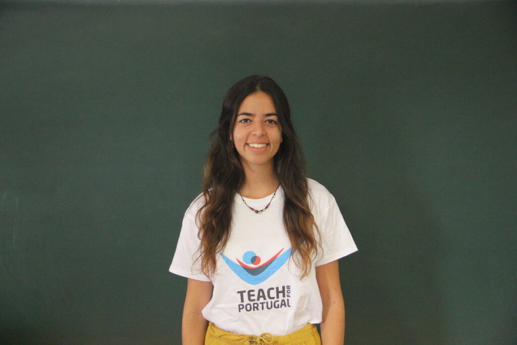 Beatriz Gaspar, Mentora 5ª Geração Teach For Portugal a usar a camisola com o logótipo da Teach For Portugal com um quadro de ardósia como fundo