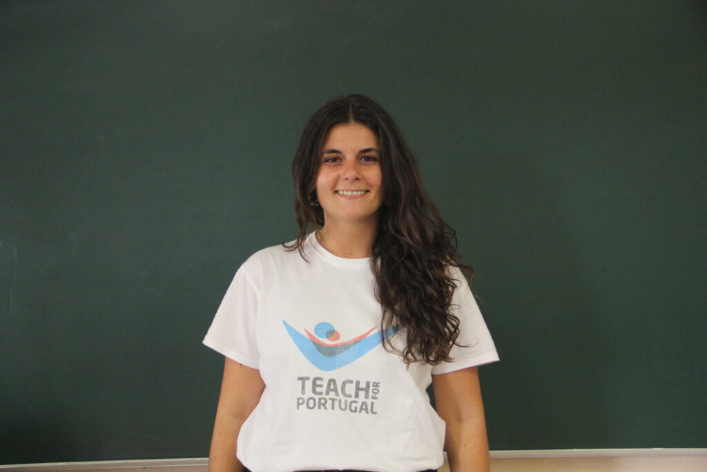 Maria Serrano, Mentora 5ª Geração Teach For Portugal a usar a camisola com o logótipo da Teach For Portugal com um quadro de ardósia como fundo