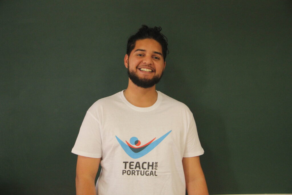 João Vítor, Mentor 5ª Geração Teach For Portugal a usar a camisola com o logótipo da Teach For Portugal com um quadro de ardósia como fundo