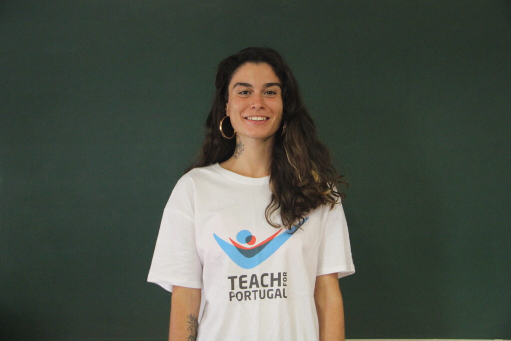 Beatriz Sousa, Mentora 5ª Geração Teach For Portugal a usar a camisola com o logótipo da Teach For Portugal com um quadro de ardósia como fundo