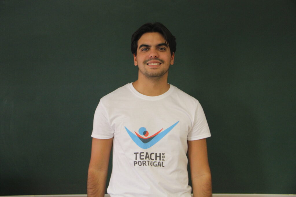 Bruno Preces, Mentor 5ª Geração Teach For Portugal a usar a camisola com o logótipo da Teach For Portugal com um quadro de ardósia como fundo