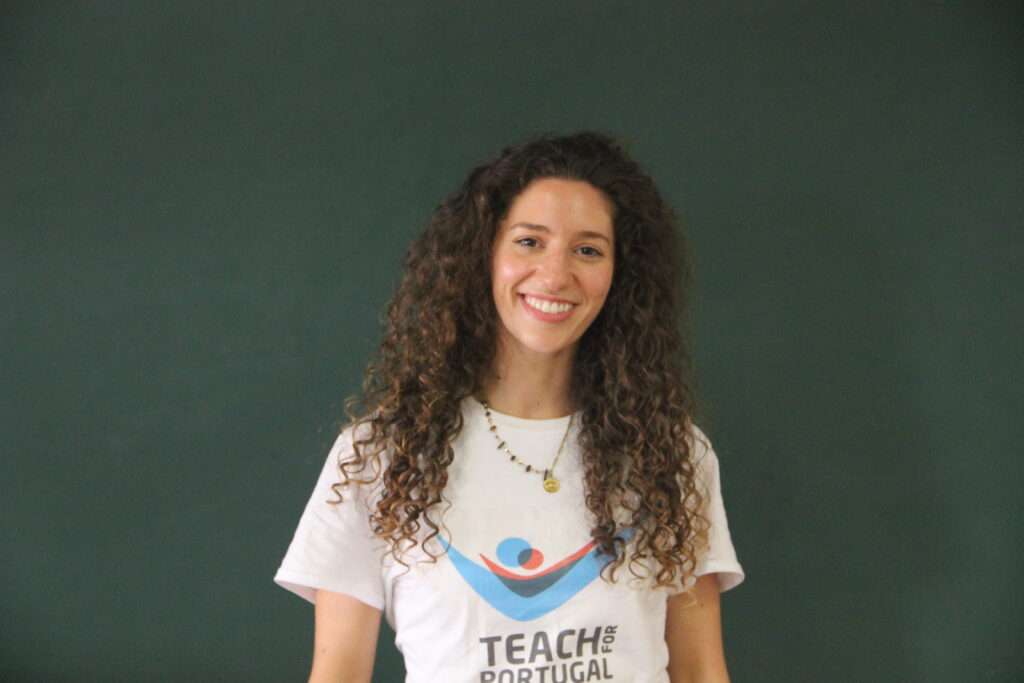 Rafaela Mendes, Mentora 5ª Geração Teach For Portugal a usar a camisola com o logótipo da Teach For Portugal com um quadro de ardósia como fundo