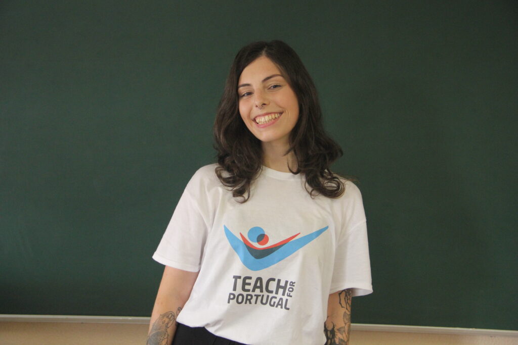 Patrícia Barbosa, Mentora 5ª Geração Teach For Portugal a usar a camisola com o logótipo da Teach For Portugal com um quadro de ardósia como fundo