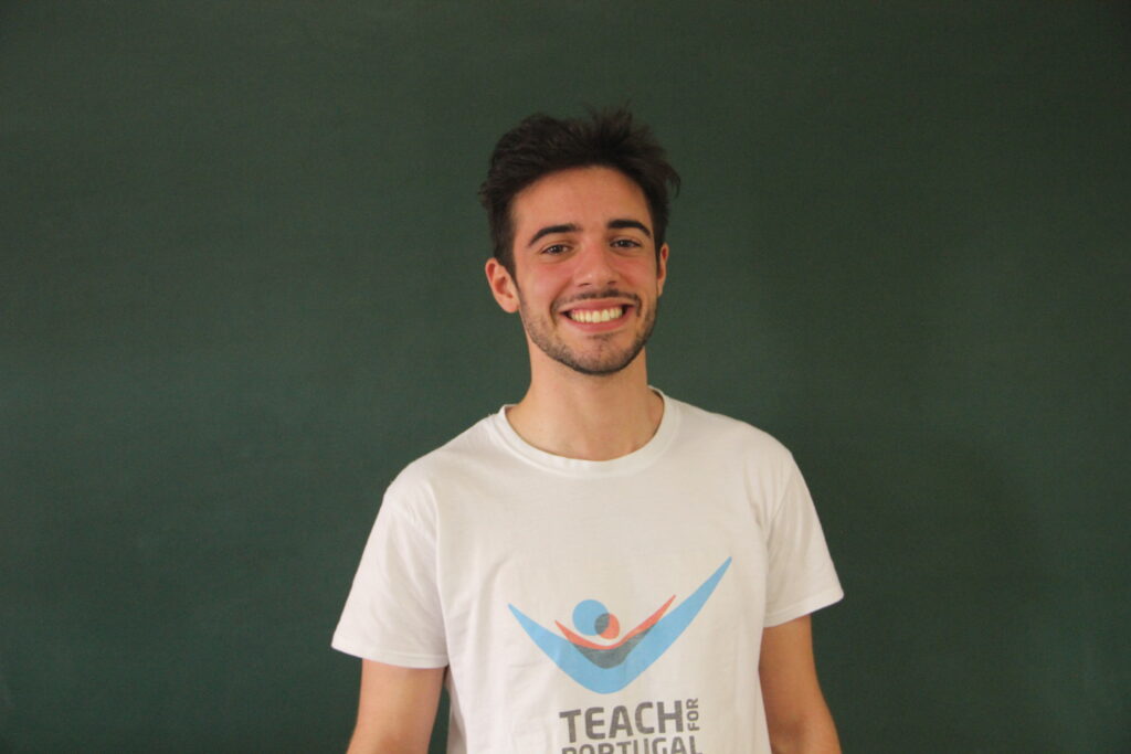 Guilherme D´Almeida, Mentora 5ª Geração Teach For Portugal a usar a camisola com o logótipo da Teach For Portugal com um quadro de ardósia como fundo