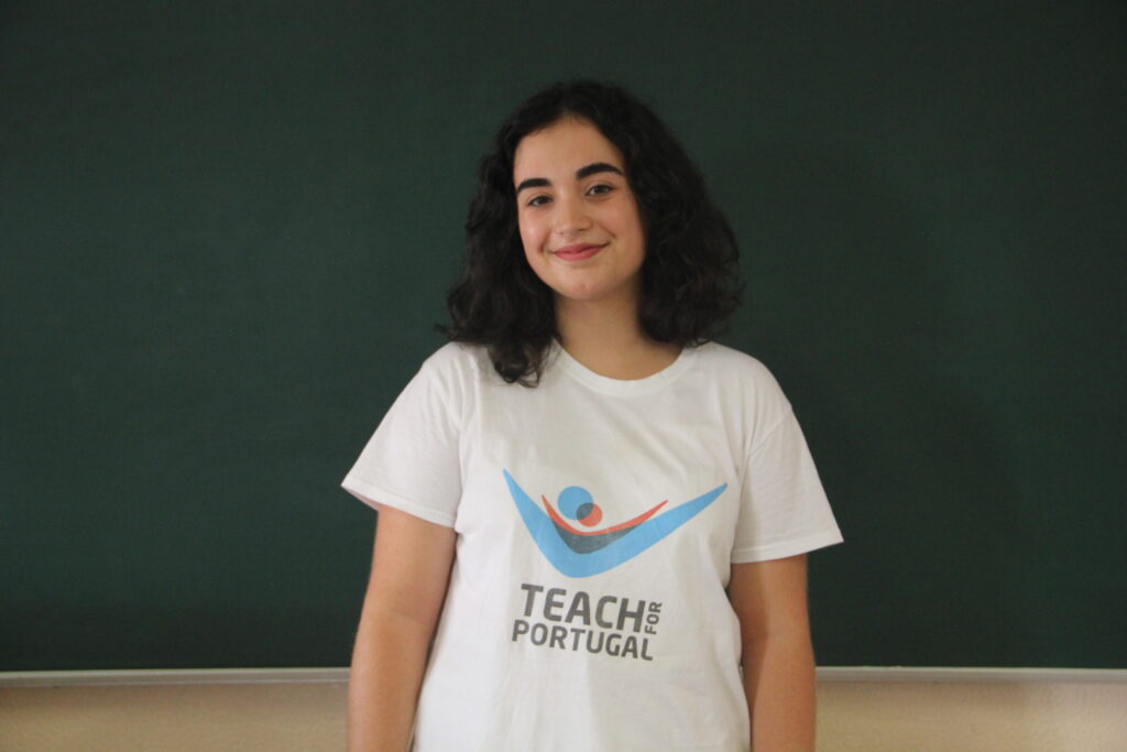 Sara Costa, Mentora 5ª Geração Teach For Portugal a usar a camisola com o logótipo da Teach For Portugal com um quadro de ardósia como fundo