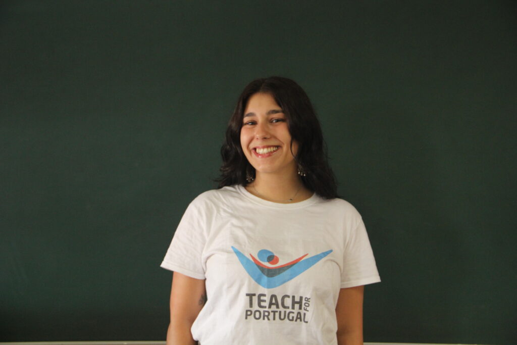 Maria Lacerda, Mentora 5ª Geração Teach For Portugal a usar a camisola com o logótipo da Teach For Portugal com um quadro de ardósia como fundo