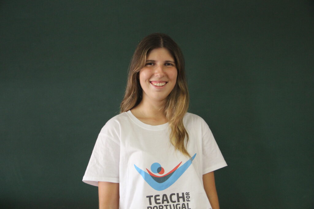 Adriana Salgado, Mentora 5ª Geração Teach For Portugal a usar a camisola com o logótipo da Teach For Portugal com um quadro de ardósia como fundo.