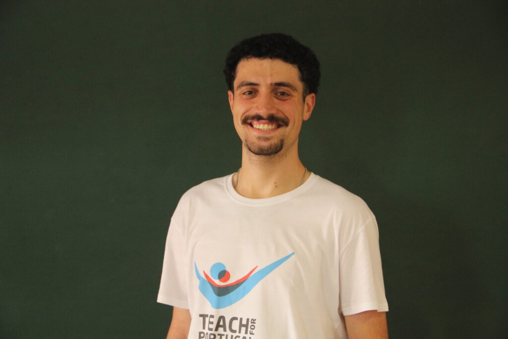 João Duarte, Mentor 5ª Geração Teach For Portugal a usar a camisola com o logótipo da Teach For Portugal com um quadro de ardósia como fundo