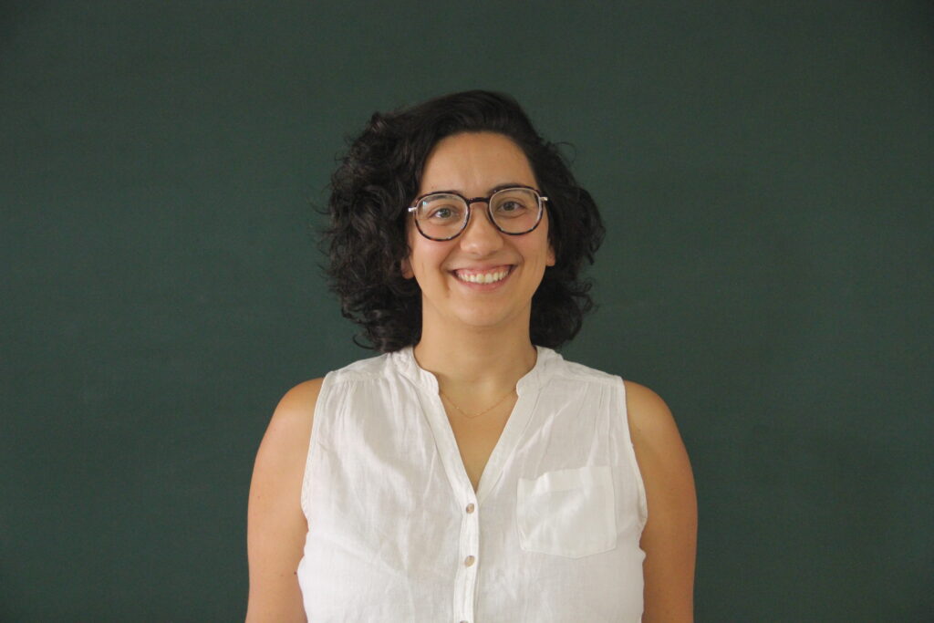 Natali Martins, a sorrir, com quadro de ardósia atrás. Representa a função de Tutora Pedagógica na Teach For Portugal