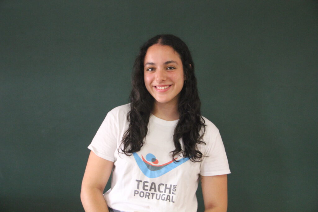 Rita Reis Rebelo, Mentora 5ª Geração Teach For Portugal a usar a camisola com o logótipo da Teach For Portugal com um quadro de ardósia como fundo