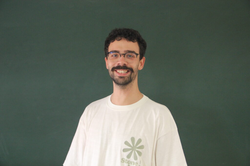 Miguel Leão, a sorrir, com quadro de ardósia atrás. Representa a função de Gestor de Recrutamento na Teach For Portugal